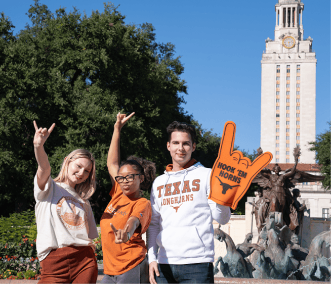 Three students gesturing Hook'em Horns in front of the Tower.