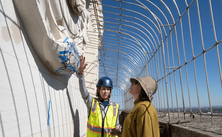 Two workers at the top of the tower discussing the exterior of the tower.