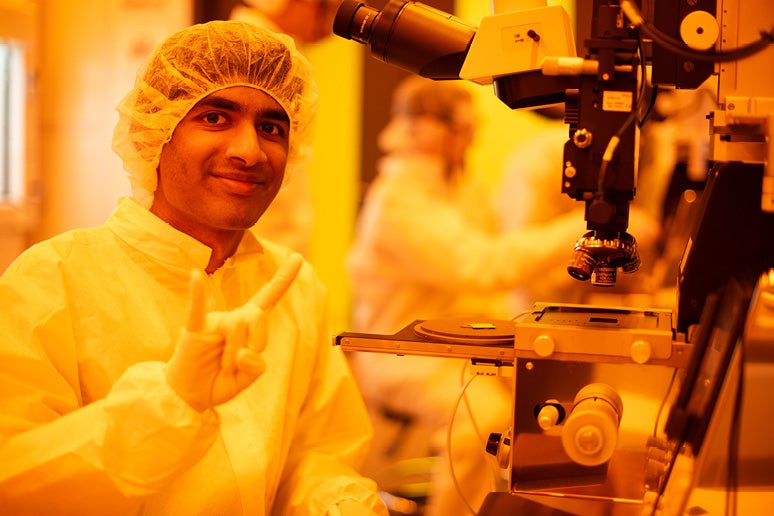 UT scientist in a lab gesturing Hook'em Horns.